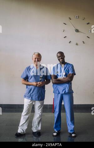 Porträt von lächelnden multirassischen Ärzten, die vor der Wand im Krankenhaus stehen Stockfoto