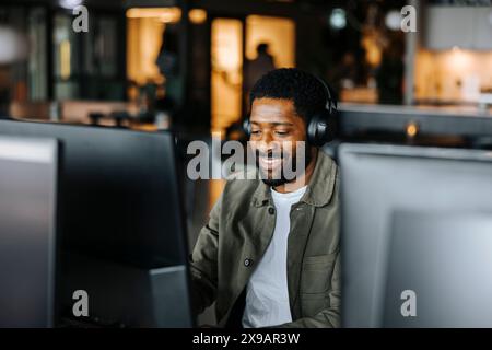 Glücklicher männlicher Unternehmer, der kabellose Kopfhörer trägt und im Büro arbeitet Stockfoto