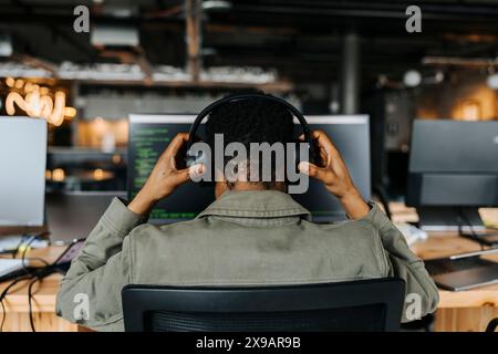 Rückansicht des Codierers mit kabellosen Kopfhörern, der am Schreibtisch im Büro sitzt Stockfoto