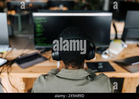 Hochwinkelansicht eines männlichen Computerprogrammierers mit Kopfhörern und Codierung im Büro Stockfoto