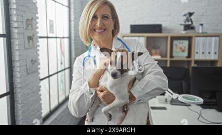 Eine reife blonde Tierärztin hält einen Hund in einer Klinik und stellt einen professionellen Tierheim-Arbeitsplatz vor. Stockfoto