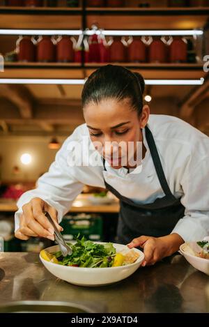 Weibliche Küchenchefin garniert Salat mit Koriander mit Pinzette in der kommerziellen Küche Stockfoto