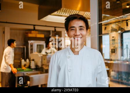 Porträt eines glücklichen männlichen Küchenchefs, der an der Tür in der kommerziellen Küche steht Stockfoto