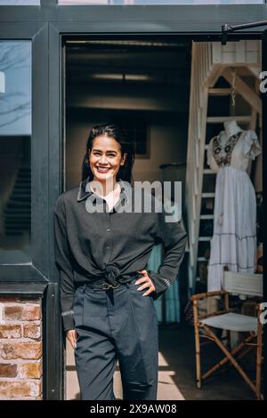 Porträt einer glücklichen Besitzerin, die mit Hand auf Hüfte am Eingang der Boutique steht Stockfoto