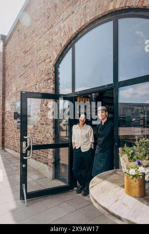 Porträt einer weiblichen Besitzerin, die mit einem männlichen Kollegen am Eingang des Cafés steht Stockfoto