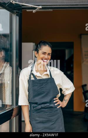 Porträt einer lächelnden weiblichen Besitzerin mit Hand auf der Hüfte, die an der Tür des Cafés liegt Stockfoto