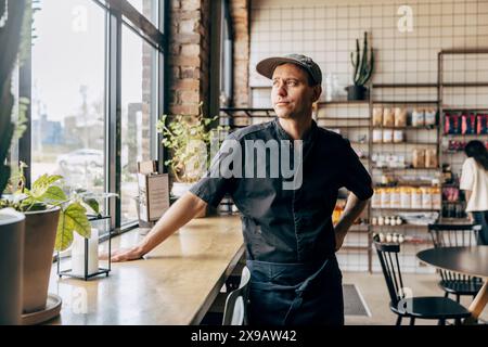 Männlicher Besitzer, der wegschaut, während er neben dem Tisch im Café steht Stockfoto