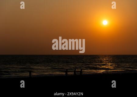 Eine ruhige Szene fängt den Sonnenuntergang über einem ruhigen Ozean mit seinem warmen Leuchten ein, das von den sanften Wellen reflektiert wird. Der Horizont teilt das Bild in TW Stockfoto