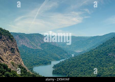 Dieses fesselnde Bild zeigt einen ruhigen Fluss, der sich durch ein majestätisches Tal schlängelt, flankiert von üppigen, grünen Bergen unter einem klaren blauen Himmel. Der Herr Stockfoto