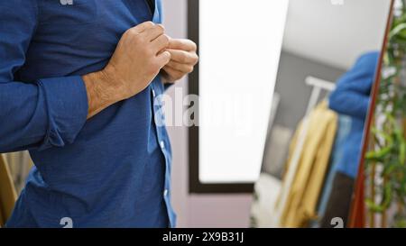 Ein junger hispanischer Mann stellt sein blaues Hemd in einem modernen Innenbereich ein. Stockfoto