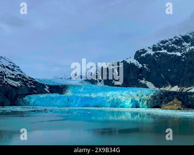 Im Glacier Bay National Park, Alaska, gibt es Eisschneewassergletscher mit schneebedeckten Bergen. Blaues Eis steht im Kontrast zu Felsformationen. Stockfoto