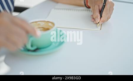 Nahaufnahme eines Mannes, der in einem Notizbuch mit einer Kaffeetasse auf einem Tisch schreibt und ein kreatives oder geschäftliches Konzept in einer ungezwungenen Umgebung repräsentiert. Stockfoto
