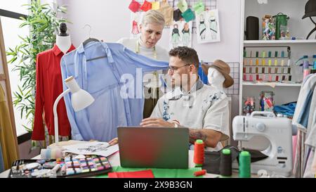 Zwei Schneider, ein Mann und eine Frau, arbeiten in einem Designraum zusammen, der mit Stoff, Nähausrüstung und Skizzen gefüllt ist. Stockfoto