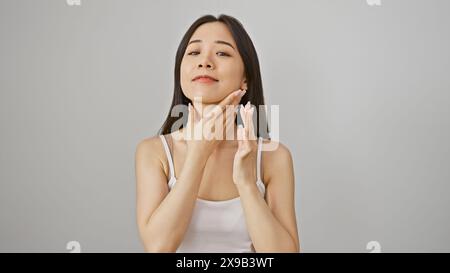 Eine schöne junge asiatische Frau mit einem ruhigen Ausdruck posiert vor weißem Hintergrund und berührt ihr Gesicht sanft. Stockfoto