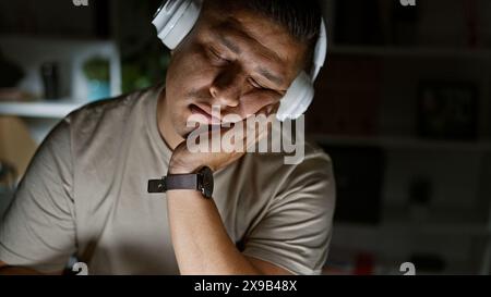 Überarbeiteter junger latin-Mann entspannt sich mit Musik und schnappt sich während eines nächtlichen Aufenthalts im Büro etwas Schlaf Stockfoto