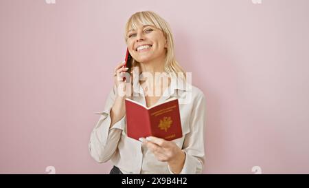 Eine fröhliche junge Frau spricht auf einem Smartphone, während sie einen roten französischen Pass hält, isoliert auf einem rosa Hintergrund. Stockfoto