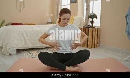 Eine ruhige junge Frau praktiziert Yoga in ihrem hellen Schlafzimmer, was Gesundheit und Achtsamkeit veranschaulicht. Stockfoto