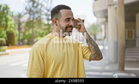 Hübscher hispanischer Mann mit Bart und Tätowierungen, der draußen in einer städtischen Umgebung lächelt. Stockfoto