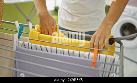 Ein Mann in einem weißen Hemd hängt die Wäsche an einem Wäscheständer im Innenbereich, um das tägliche Leben im Haushalt zu veranschaulichen. Stockfoto