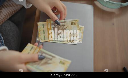 Eine junge kaukasische Frau zählt an einem Tisch drinnen norwegische Kronen, die Finanzen und das häusliche Leben darstellen. Stockfoto