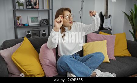 Eine junge kaukasische Frau tanzt fröhlich in einem gemütlichen Wohnzimmer und verkörpert Freizeit und Entspannung zu Hause. Stockfoto