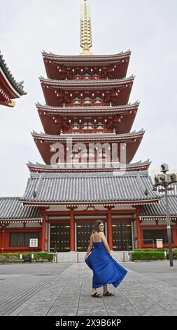 Die sprudelnde hispanische Frau tanzt fröhlich und dreht sich in wunderschönem Kleid inmitten der herrlichen Architektur des Senso-JI-Tempels in tokio. Sie ist durch japan gereist Stockfoto