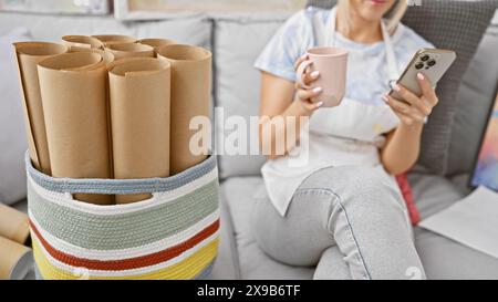 Eine vertiefte Künstlerin trinkt Kaffee, benutzt Smartphone in der Hand, taucht in die Kunst auf Leinwand im Studio ein Stockfoto