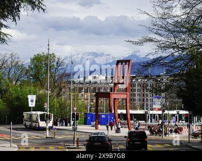 Menschen, die den Giant Sessel mit gebrochenem Bein sehen, gegenüber dem Palast der Nationen, mit schneebedeckten Bergen im Hintergrund, Genf, Schweiz. Stockfoto