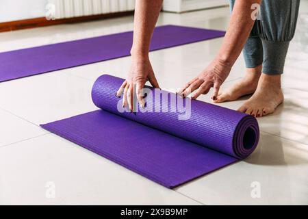 Seniorin, die ihre Trainingsmatte nach einem Yoga-Kurs aufrollte. Stockfoto