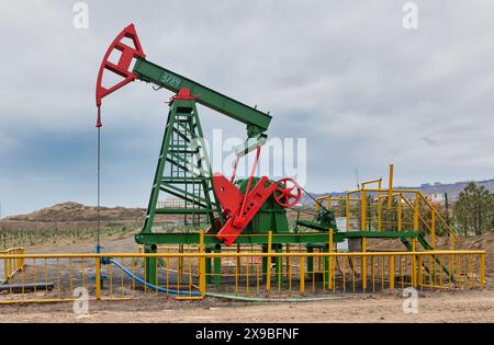 Ein in Betrieb befindlicher grüner und roter Ölpumpjack, umgeben von gelben Zäunen, vor einem bewölkten Himmel, in Baku, Aserbaidschan Stockfoto