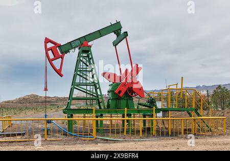 Ein in Betrieb befindlicher grüner und roter Ölpumpjack, umgeben von gelben Zäunen, vor einem bewölkten Himmel, in Baku, Aserbaidschan Stockfoto