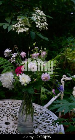 Gartenblumen in einer Glasvase auf einem weißen Tisch. Weißer Gartenstuhl. Holunderblüten. Stockfoto