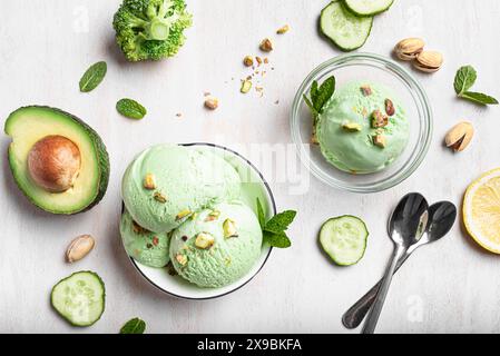 Grüne Avocado-Kokos-Eiskugeln in Schüsseln und Zutaten auf weißem Holzhintergrund, Blick von oben. Trendiges veganes Eis mit grünem Gemüse. Stockfoto