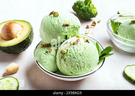 Grüne Avocado-Kokos-Eislöffel mit Pistazien in Schüsseln und Zutaten auf weißem hölzernem Hintergrund, Blick von oben. Trendiges veganes Eis mit gre Stockfoto