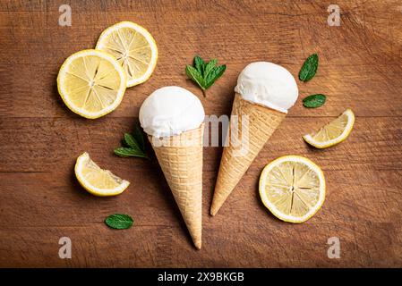 Schaufel Zitroneneis in Waffelkegel und Zitronenscheiben auf hölzernem Hintergrund, Blick von oben. Hausgemachtes veganes Zitronenkos. Stockfoto