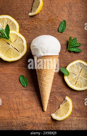 Eine Schaufel Zitroneneis in Waffelkegel und Zitronenscheiben auf hölzernem Hintergrund, Blick von oben. Hausgemachtes veganes Zitronenkos. Stockfoto