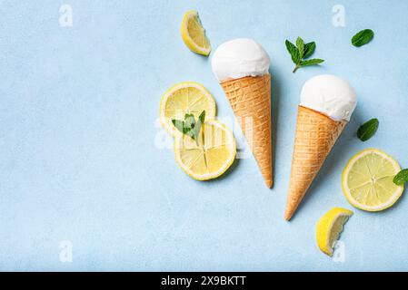 Löffel Zitroneneis in Waffelkegel und Zitronenscheiben auf hellblauem Hintergrund, Draufsicht, Kopierraum. Trendiges, kreatives Layout. Stockfoto