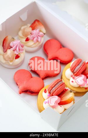 Gebäckset zum Valentinstag oder für jeden romantischen Tag, verpackt in einer Pappschachtel. Herzförmige Makronen und Mini-Kuchen Stockfoto