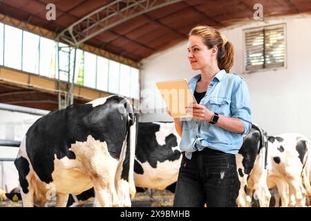 Selbstbewusste Tierbauerin arbeitet in Viehzuchtbetrieben mit einem digitalen Tablet und sammelt Cloud-Daten von Tieren. Weibliche Landwirte und Kühe. Stockfoto