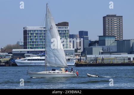 Portsmouth, England, 12. Mai 2024. Vom Gosport Harbour aus: Ein großes weißes Segelboot auf ruhigem Wasser, das ein kleines Schlauchboot schleppt. Stockfoto