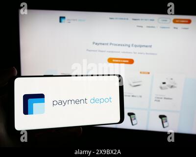 Person mit Smartphone und Logo des US-Kartenverarbeitungsunternehmens Payment Depot (Stax Payments) vor der Website. Schwerpunkt auf dem Display des Telefons. Stockfoto