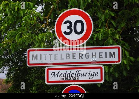 PRODUKTION - 29. Mai 2024, Frankreich, Mittelbergheim: Das Ortszeichen Mittelbergheim steht am Ortseingang und trägt darunter auch den elsässischen Namen „Meddelbarige im ELSASS“. In den Sonderregelungen des lokalen Rechts im Elsass und Lothringen heißt es, dass in den Regionen, die nach dem Ersten Weltkrieg wieder Teil Frankreichs wurden, deutsche Vorschriften in vielen Bereichen des gesellschaftlichen Lebens eingehalten wurden. Das reicht vom Jagdrecht über religiöse Praxis und Krankenversicherung bis hin zu Kataster und Verbänden. Die Grenzregion hat derzeit Schwierigkeiten sicherzustellen, dass das lokale Recht nicht untergraben wird Stockfoto