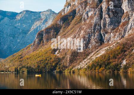 Ein kleines gelbes Kanu gleitet an einem ruhigen Herbsttag über atemberaubende Berge, die am Ufer des Bohinj-Sees in Slowenien auf das Wasser treffen Stockfoto