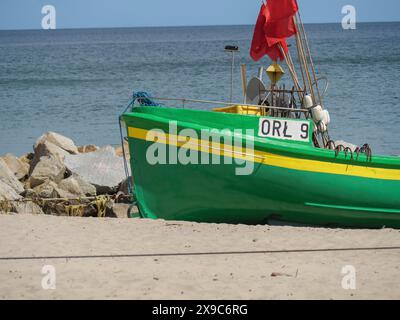 Ein grünes Fischerboot mit roter Flagge liegt am Strand in der Nähe von Felsen, grüne und gelbe Fischerboote am Strand in Polen, sopot, polen Stockfoto