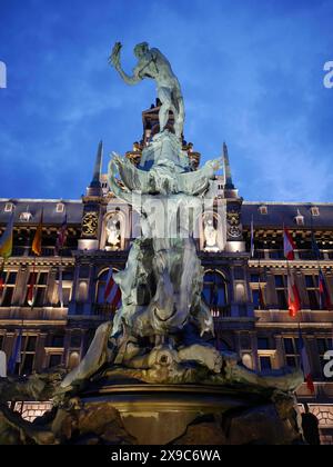 Statue auf einem Brunnen vor einem beleuchteten historischen Gebäude bei Nacht, barocke Architektur und Flaggen, der historische Marktplatz von Antwerpen Stockfoto