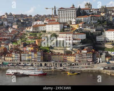 Blick auf eine hügelige Stadt mit farbenfrohen Häusern und Booten am Ufer unter bewölktem Himmel, Frühling in der Altstadt von Porto auf dem Douro mit historischem Stockfoto