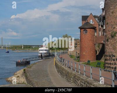 Historischer Hafen mit Backsteinmauern, Booten und einem Pier an einem Fluss, rheinpromenade von Rees mit historischen Gebäuden, grüne Bäume, rees, deutschland Stockfoto