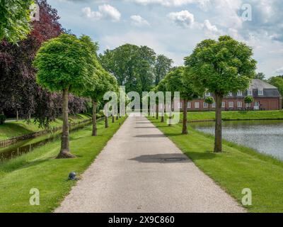 Lange, von Bäumen gesäumte Allee mit gepflegtem Grün auf beiden Seiten, die zu einem historischen Gebäude, einer alten roten Backsteinburg mit Türmen und einem großen Park mit führt Stockfoto