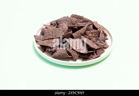 Organische blaue Maistortilla Chips auf Platte auf hellgrünem Hintergrund. Gesunder Knuspriger Snack Mit Meersalz Gewürzt. Horizontale Ebene Entwerfen. Stockfoto