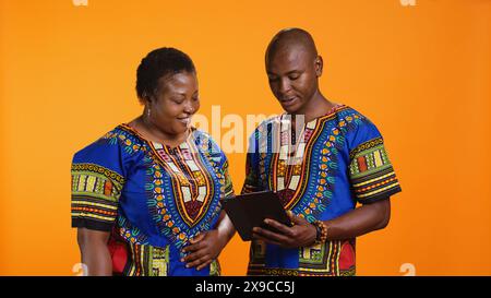 Ethnische Personen, die auf Social-Media-Webseiten navigieren, Nachrichten überprüfen und Fotos vor orangefarbenem Hintergrund ansehen. afroamerikanische Männer und Frauen, die Online-Websites im Studio scrollen. Stockfoto
